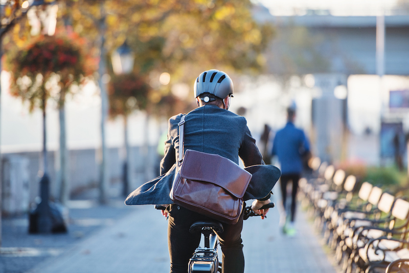 a man riding a bike on a park path with a helmet and brown work bag